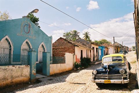 Church alongside cool Cuban car on cobblestone road